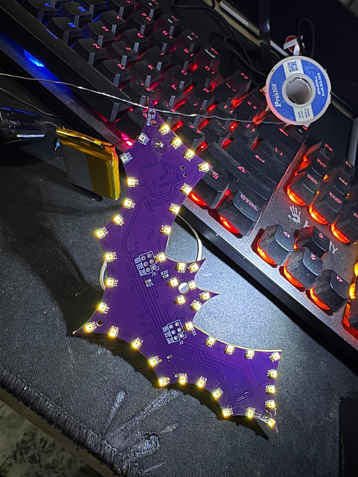 Assembled bat-shaped badge PCB showing the RGB LED ring, reference designators and I²C header footprints