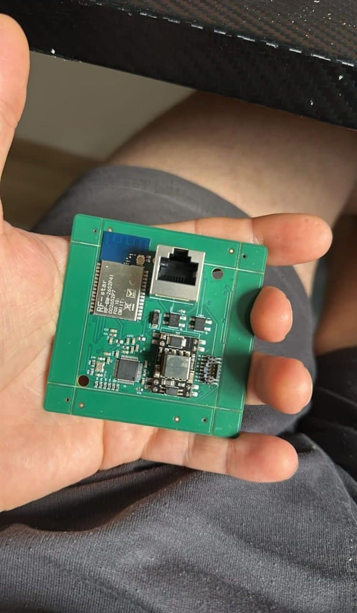 The compact square gateway PCB held in a hand for scale, with mounting holes at each corner